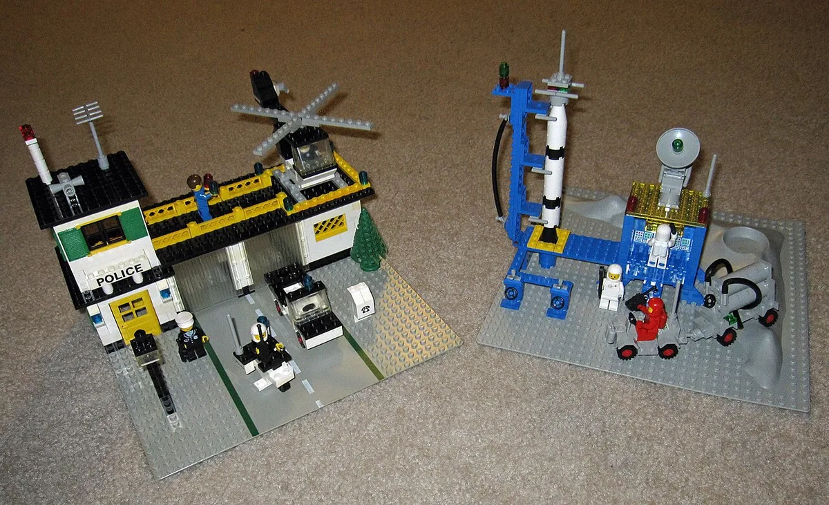 Twee gebouwde LEGO-sets uit de jaren tachtig naast elkaar: een politiebureau met voertuigen en een ruimtevaartbasis met een raket op een lanceerplatform.