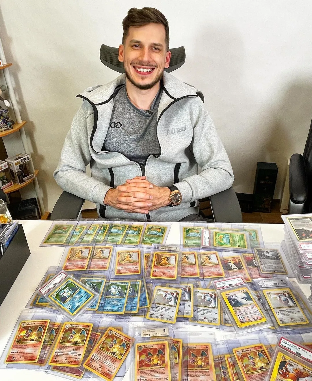 Een man zit achter een tafel waarop tientallen Pokémonkaarten in doorzichtige beoordelingshouders naast elkaar zijn uitgestald.