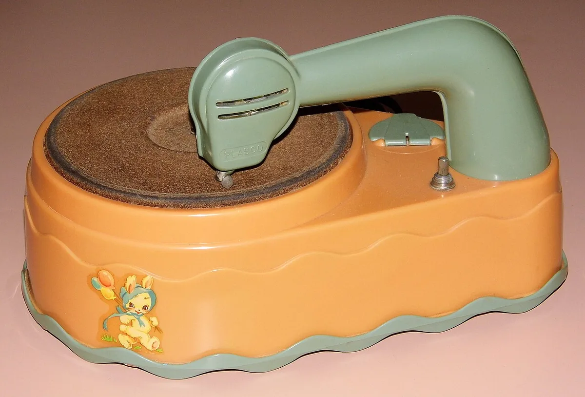 Een vintage kinderplatenspeler van oranje en groen kunststof met een versleten draaischijf en een groene toonarm.